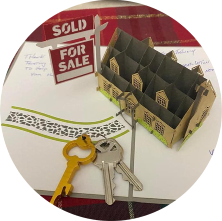 For sale sign, miniature model home and keys laying on a table